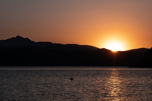 Beautiful sunrise over a calm bay with serene mountains in the background, creating a peaceful landscape.