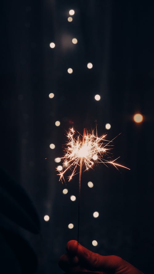 A person holding a sparkler in front of a dark background