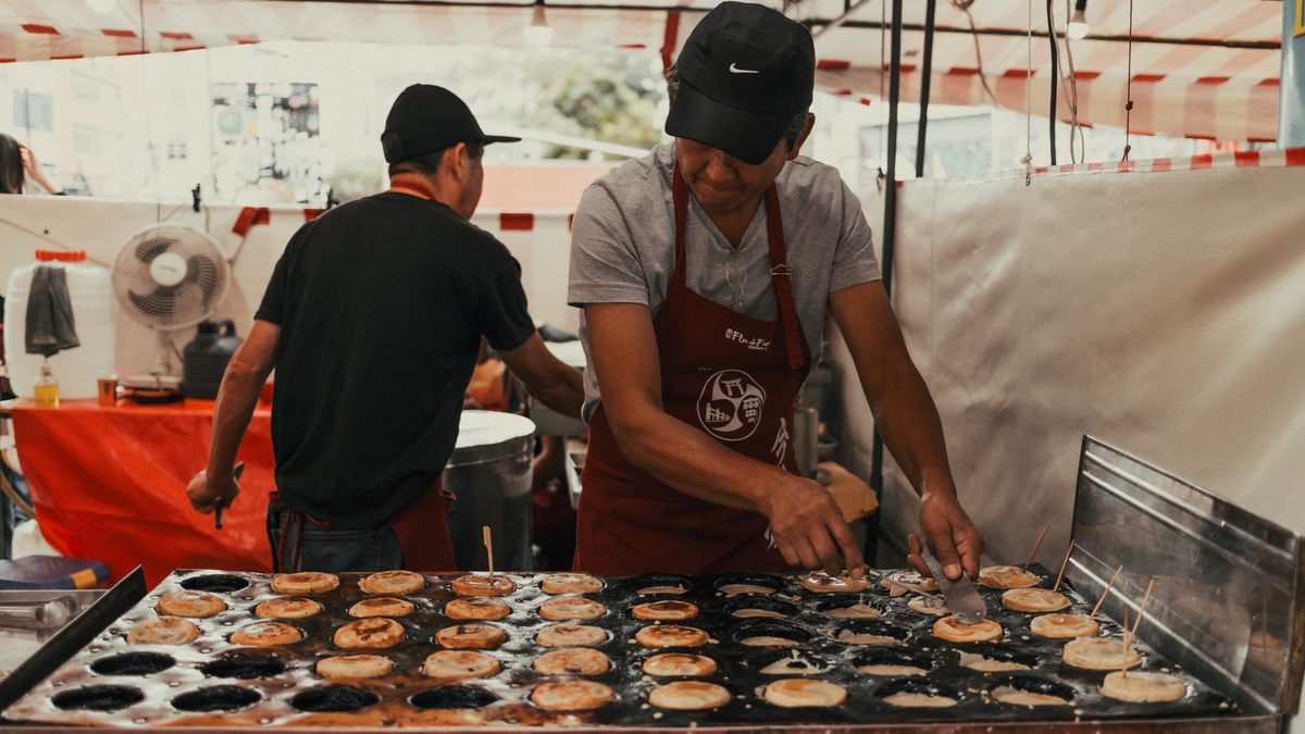 Asian street food vendor preparing snacks outdoors at a bustling market.