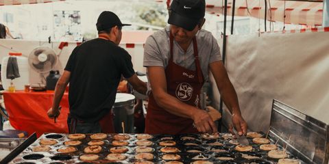 Asian street food vendor preparing snacks outdoors at a bustling market.
