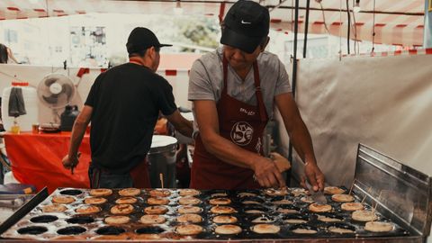 Asian street food vendor preparing snacks outdoors at a bustling market.