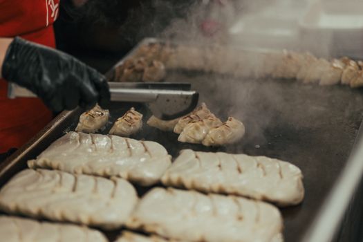 Close-up of a chef cooking dumplings on a griddle in a commercial kitchen.