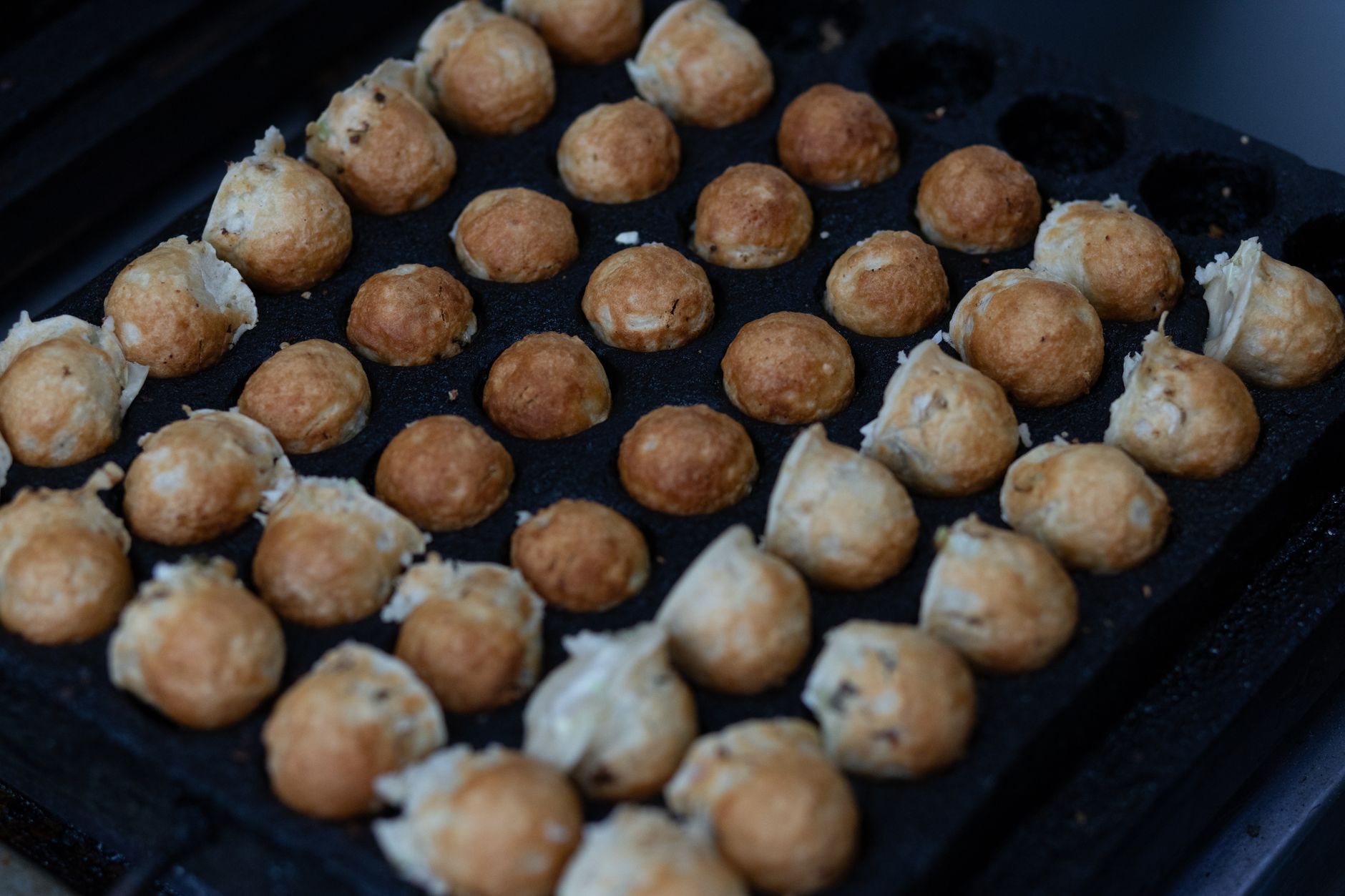 Close-up of Japanese takoyaki balls cooking on a grill, crispy and golden.