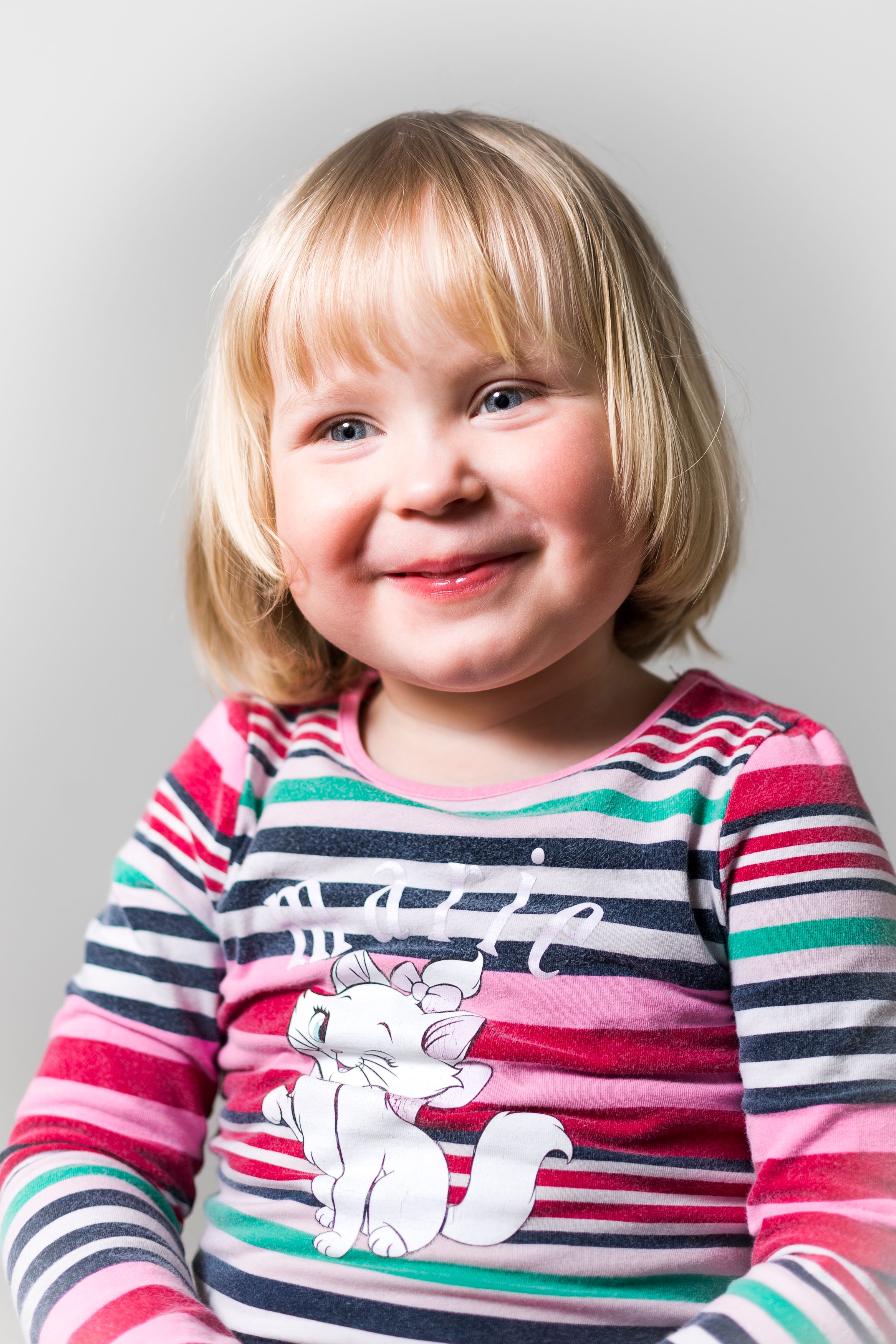 Adorable blond child smiling in a colorful striped shirt with a cat print.
