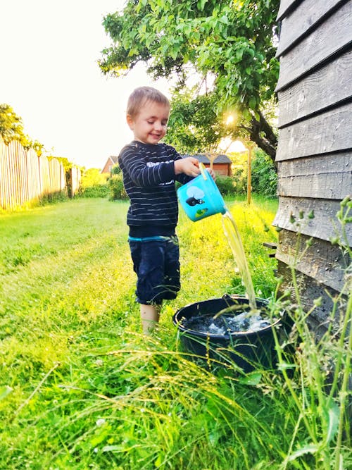 Side View Photo of Happy Boy Playing With Water on Side of a Wooden House