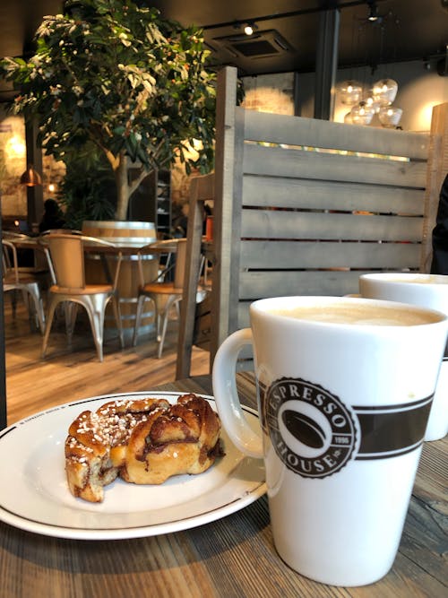 Cinnamon Roll on a Ceramic Plate Next to a Latte