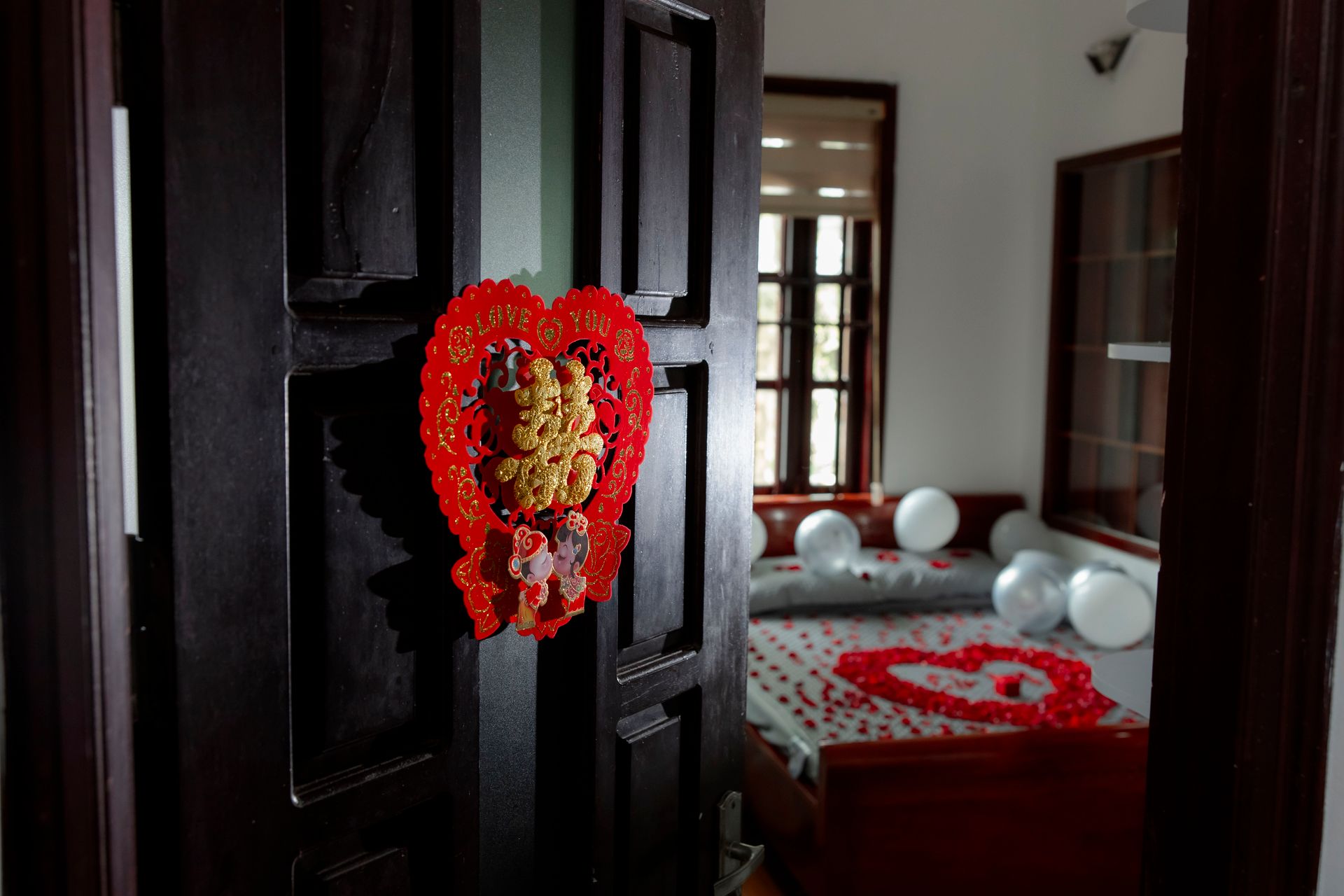 A romantic bedroom setup with red and white decor, including heart-shaped details and balloons.