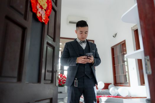 A groom in a suit checks his smartphone indoors, preparing for a wedding ceremony.
