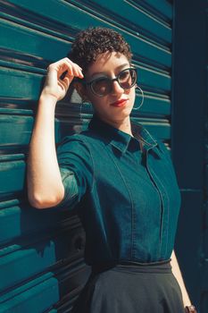 Trendy woman in denim shirt with curly hair and sunglasses against a blue background.