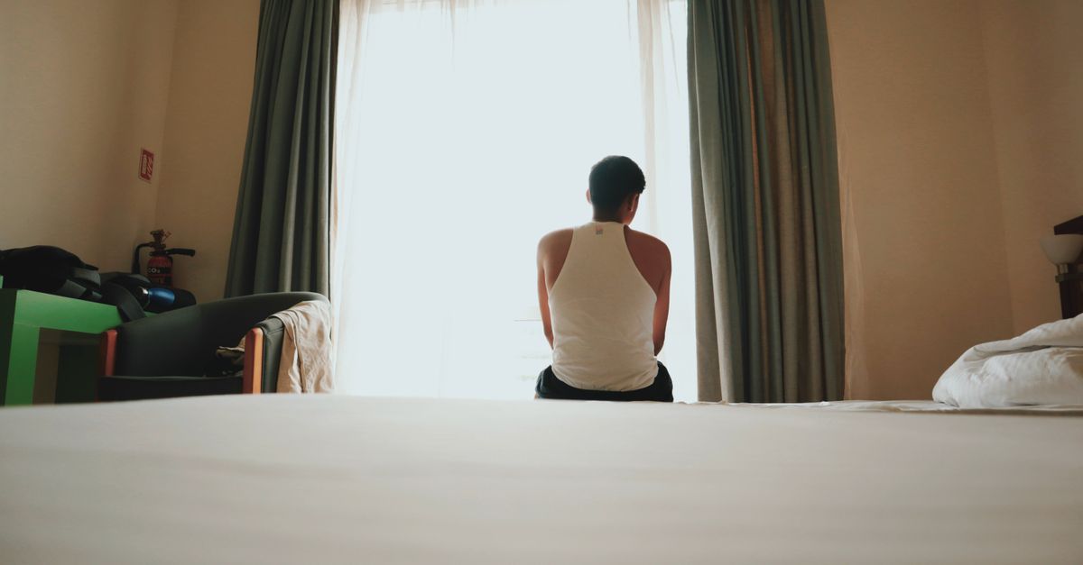 Person sitting quietly on a bed facing a window