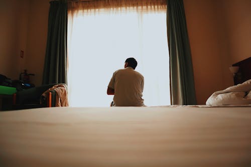 A man sitting on a bed looking out a window