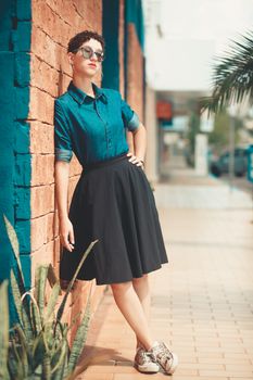 Chic woman in stylish outfit leans against a colorful brick wall during the day.