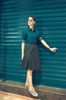 Fashionable woman in a jean shirt and skirt poses against a blue urban wall. Modern look.