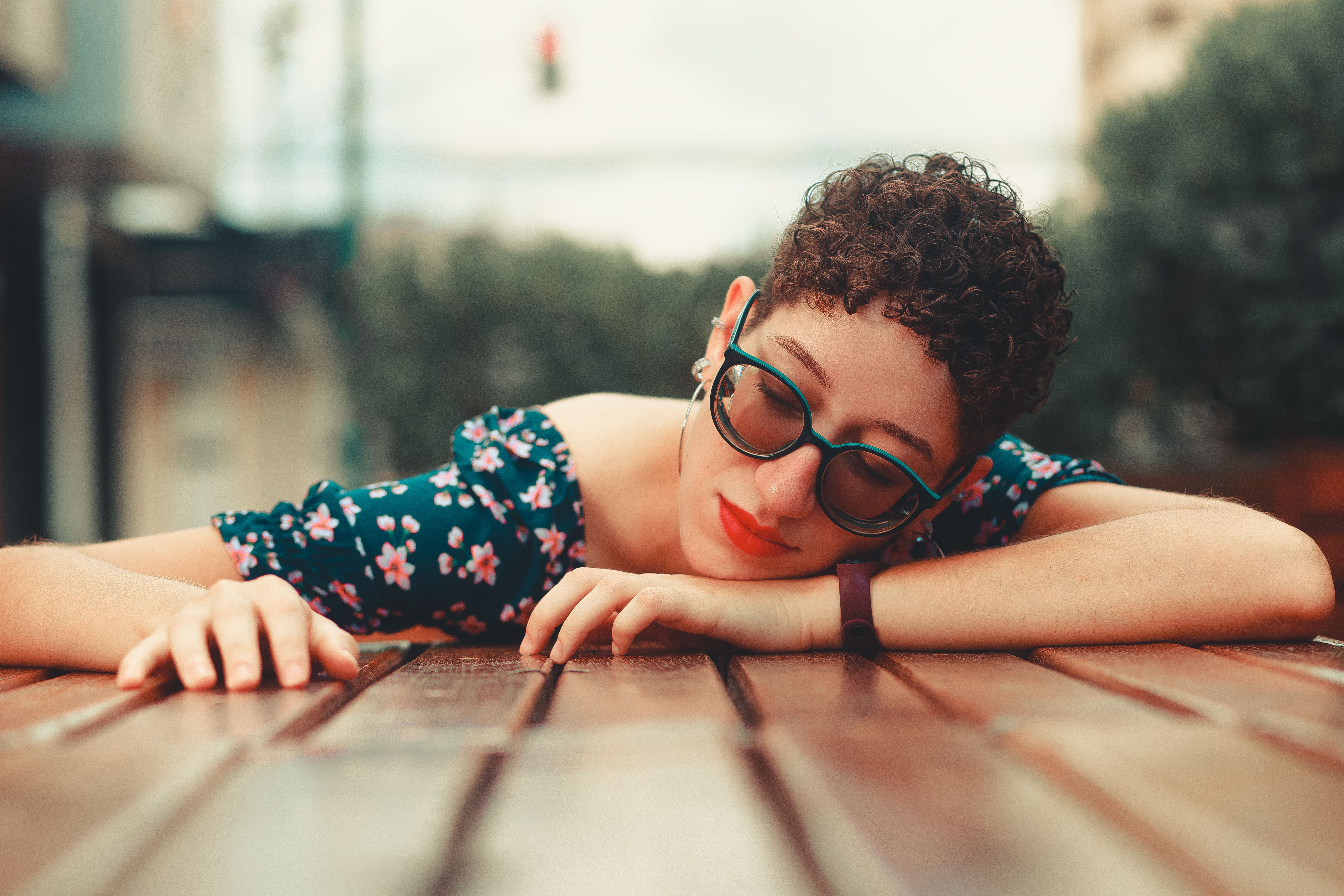 Woman with short curly hair and sunglasses lounging on a wooden table outdoors.