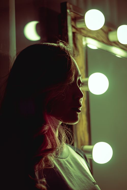 Free Silhouette of a woman in a moody setting before a vanity mirror with glowing lights. Stock Photo