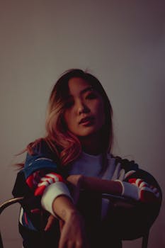 一位成年女性穿着时尚服装，在弱光下坐在椅子上摆姿势