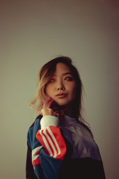 一位亚洲女性身着时尚运动衫，在中性背景下展现现代时尚的肖像