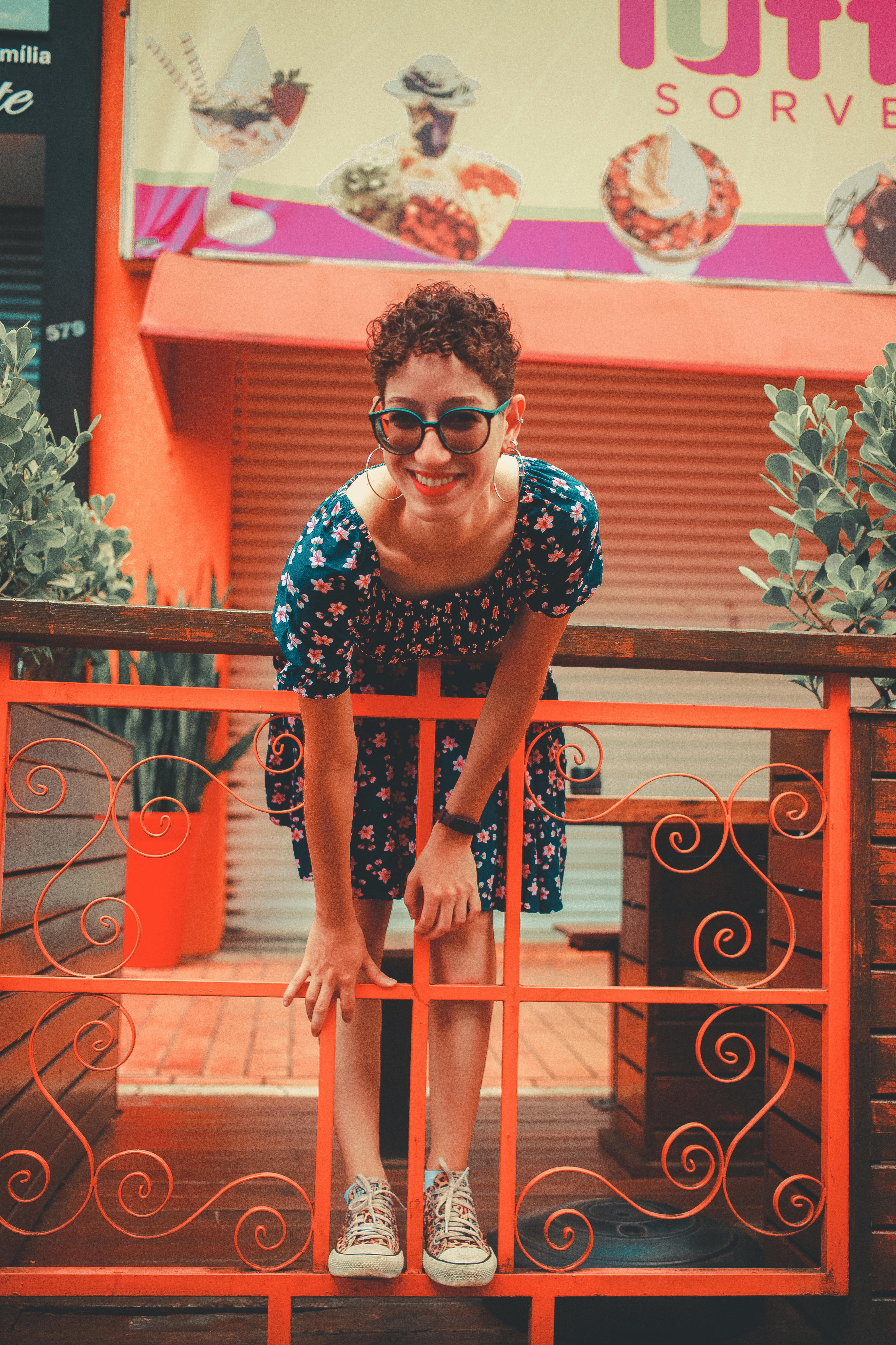 Cheerful woman in floral dress and sunglasses posing playfully on a colorful urban patio.