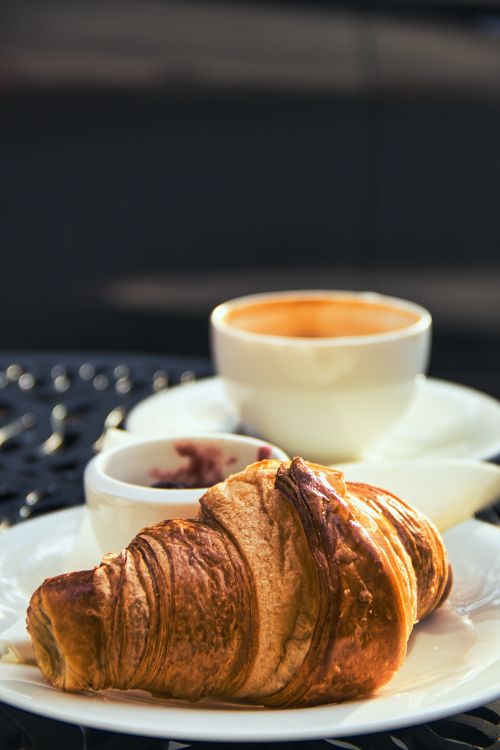 Free Enjoy a delicious breakfast with a croissant, coffee, and jam in a cozy Berlin café setting. Stock Photo