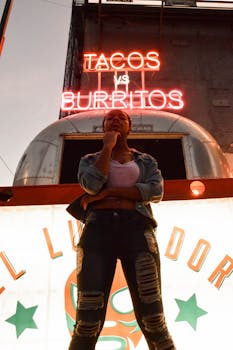 霓虹塔可招牌下，一名女子若有所思地站在城市环境中