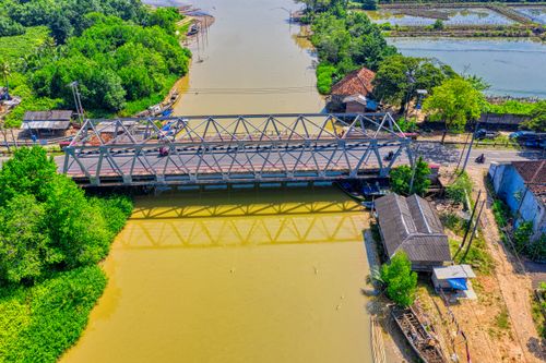 Free Aerial image of a bridge spanning a tranquil river surrounded by lush greenery and rural buildings. Stock Photo