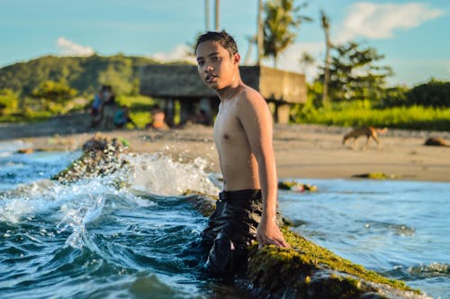 Topless Boy Sitting on Rock Beside Body of Water Viewing Mountain