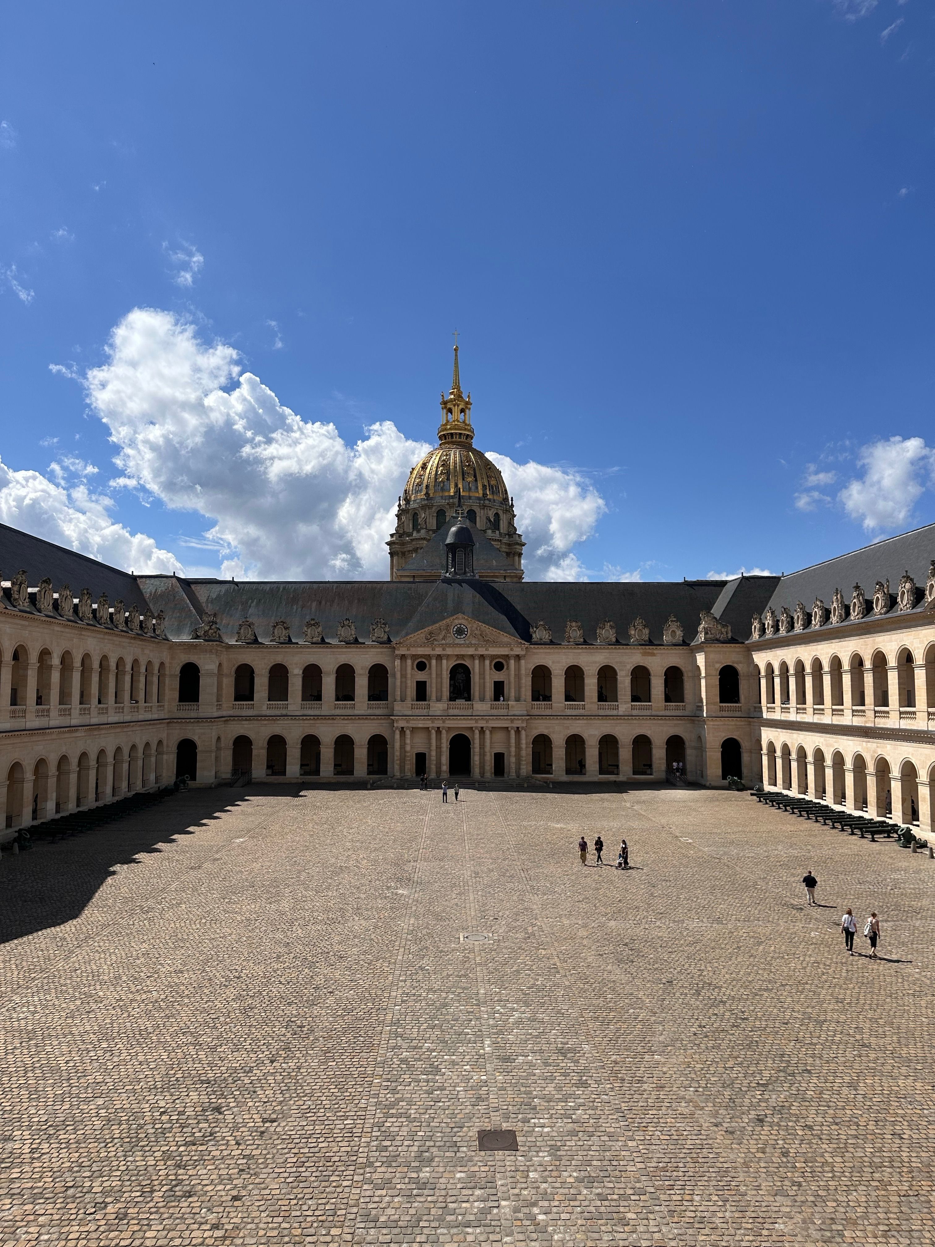 Elegant view of Les Invalides courtyard with golden dome under a bright blue sky in Paris.
