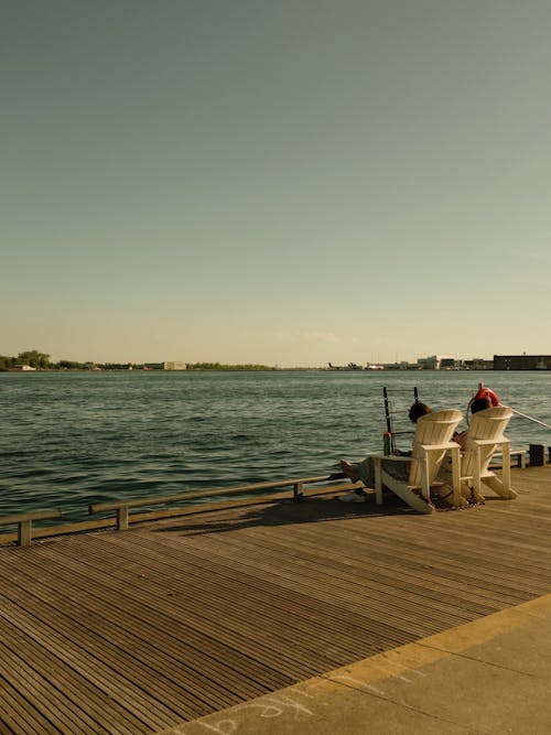 Two people sitting on a dock looking out at the water