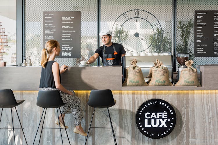 Woman Sitting On Bar Chair Near Barista