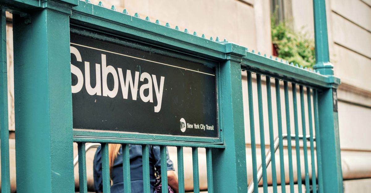 Close-up of New York City subway entrance featuring a green railing and people.