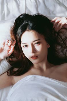 A peaceful morning portrait of a woman lying gracefully on a white bed, exuding relaxation.