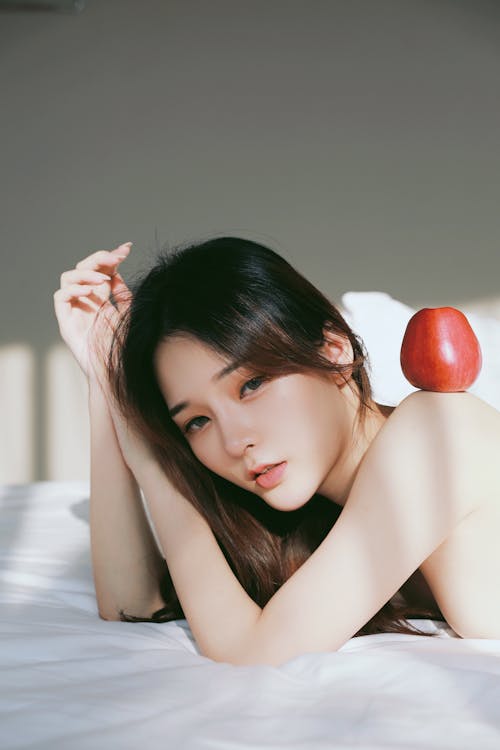 A woman laying on a bed with an apple on her head
