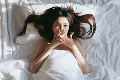 Free Top view of a young Asian woman resting in bed, sunlit morning, relaxed and serene. Stock Photo