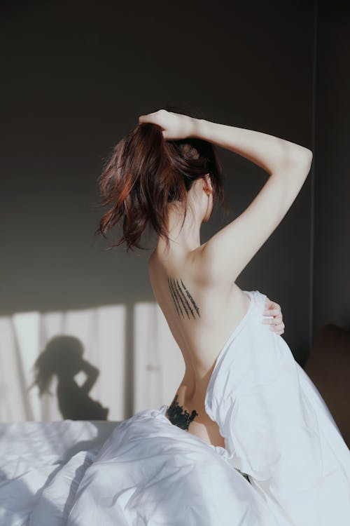 A woman with a tattoo on her back is laying in bed