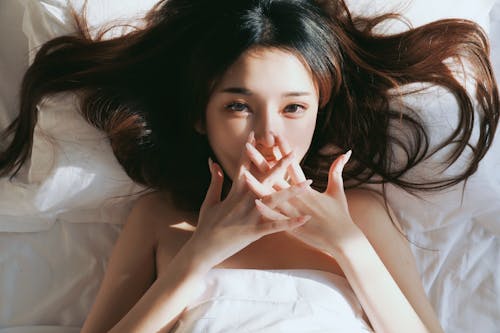 A woman laying in bed with her hands covering her mouth