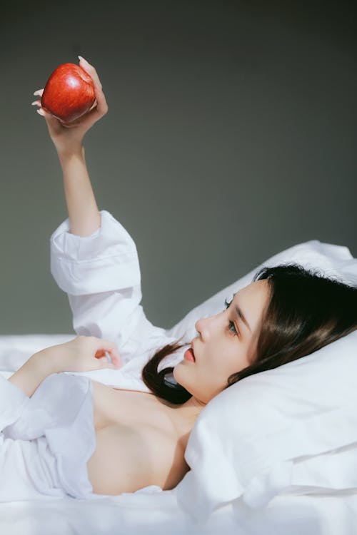A woman laying in bed holding an apple
