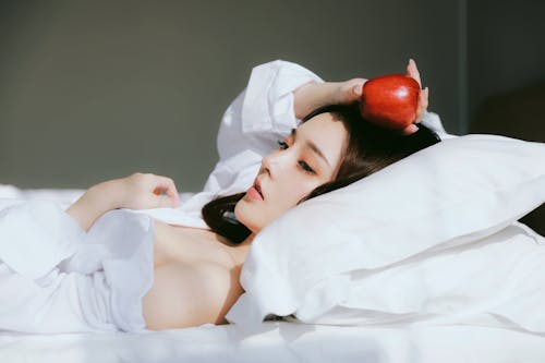 A woman laying in bed with an apple on her head