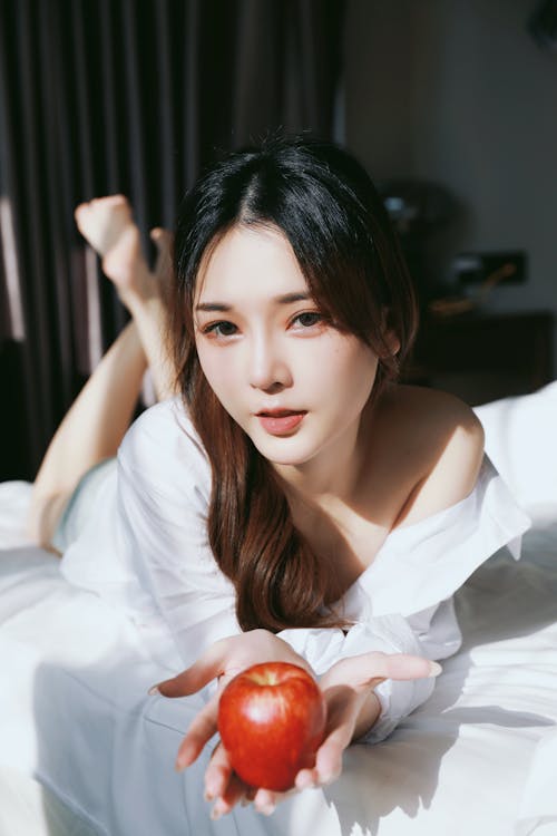 A woman laying on a bed holding an apple
