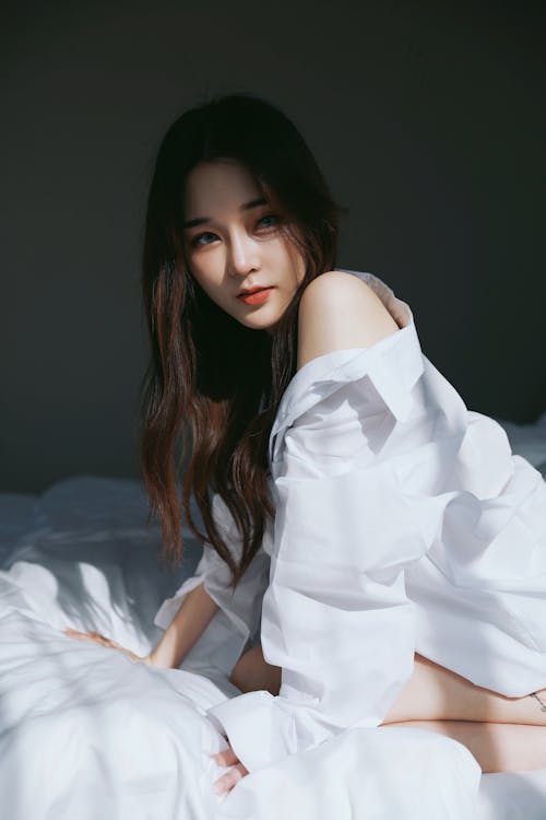 A woman in white shirt sitting on bed