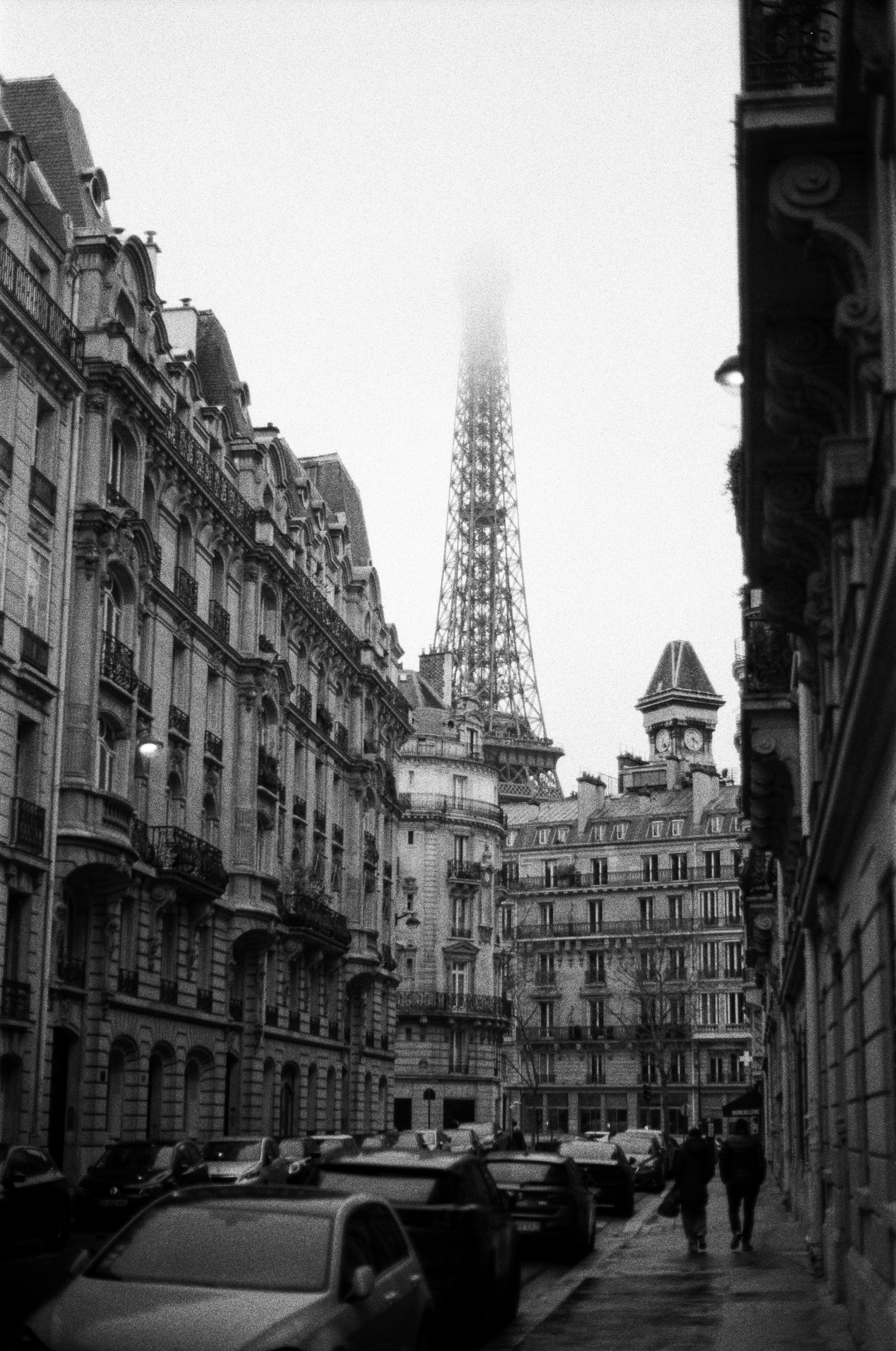 Black and white view of a Paris street with the Eiffel Tower shrouded in fog, capturing urban charm.