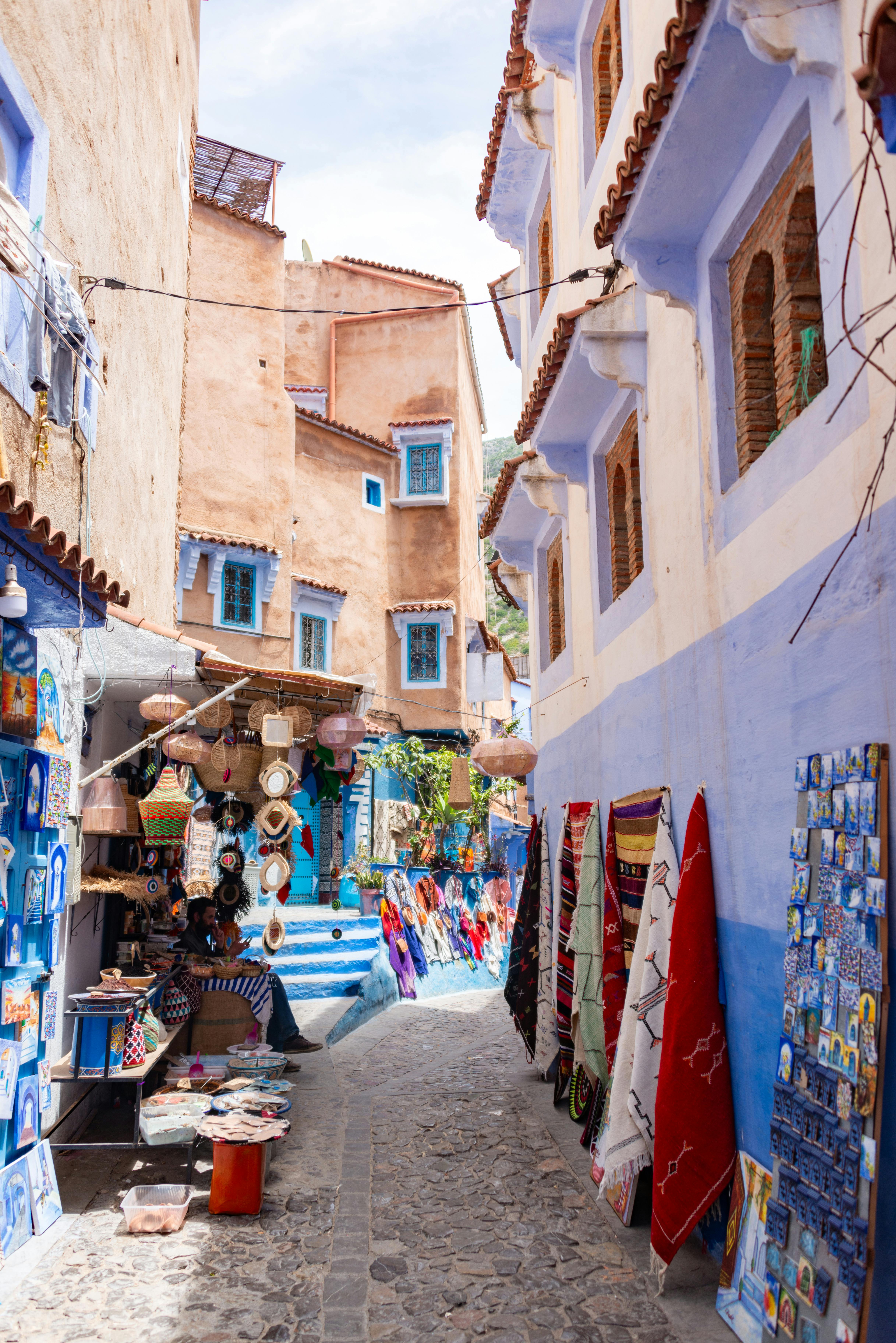 Explore the bustling market alley in Chefchaouen, Morocco, filled with colorful textiles and pottery.