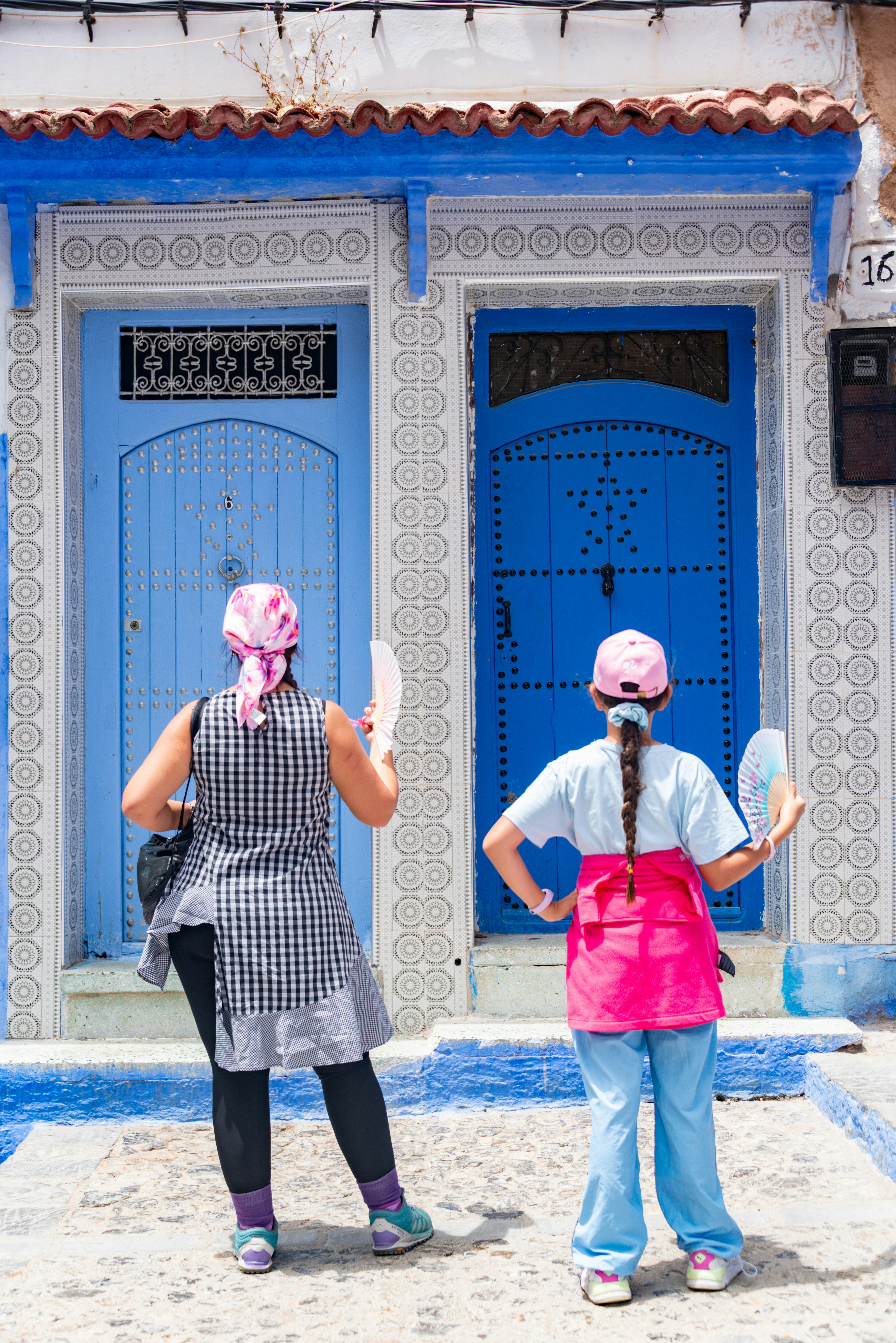 Two women stand in front of traditional blue doors in Morocco, adding vibrant color to their exploration.