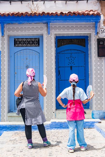 Two women stand in front of traditional blue doors in Morocco, adding vibrant color to their exploration.