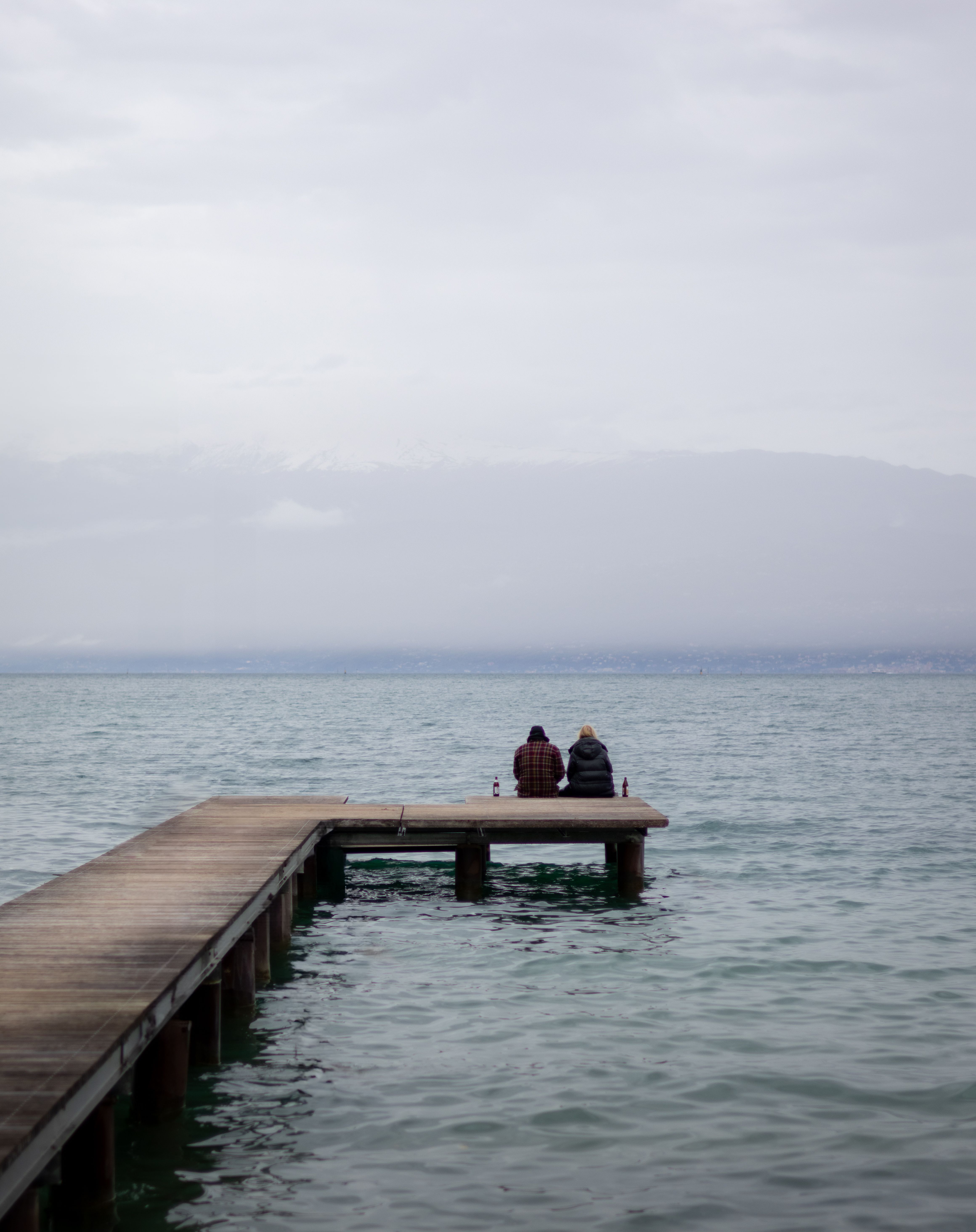 A couple enjoys a tranquil moment on a pier overlooking Lake Garda, Italy, on an overcast day.