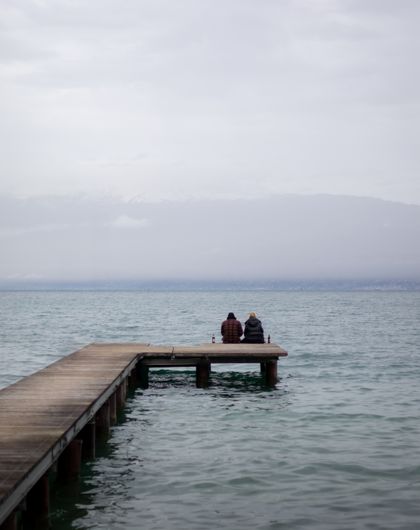 Two people sitting at the end of a lake pier, photo by Florian Suess on Pexels