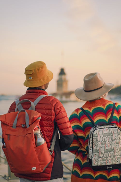 Two people wearing hats and backpacks looking at the ocean
