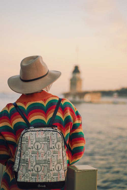 A woman in a hat and sweater is looking at the water