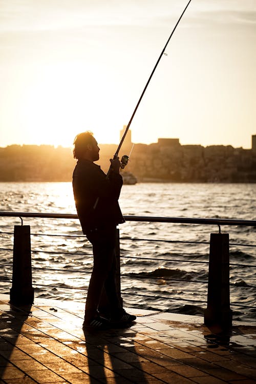 A man is fishing on the water at sunset