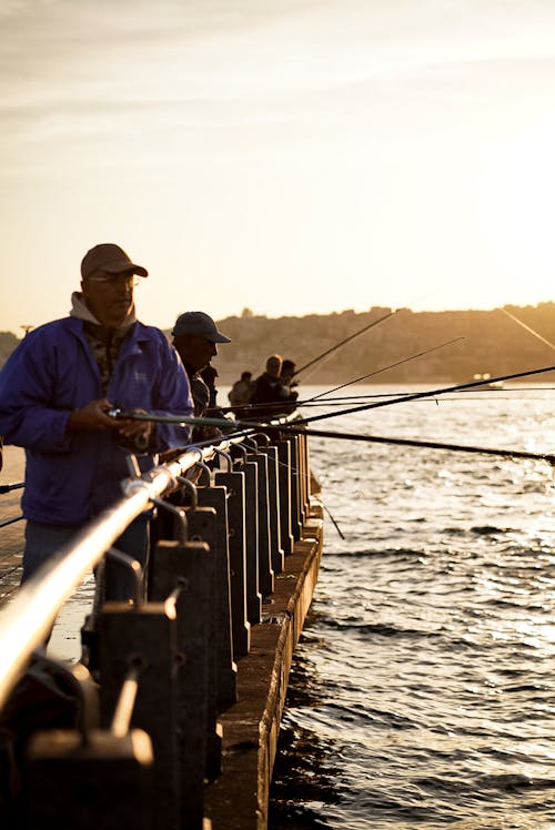 A man fishing on a pier at sunset