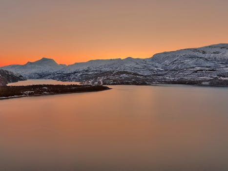 Scenic view of snow-covered mountains reflecting golden sunset near a lake in Sweden.